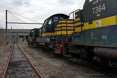 Row of green-and-yellow locomotives on an outdoor track beneath cloudy sky.