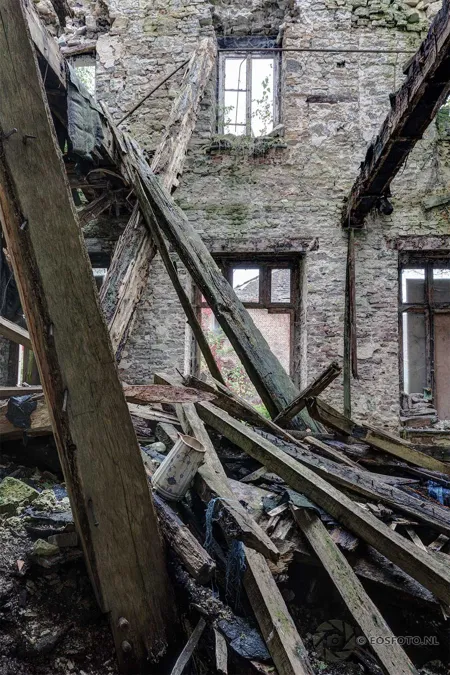 Collapsed wooden floor sections in a tall damaged room