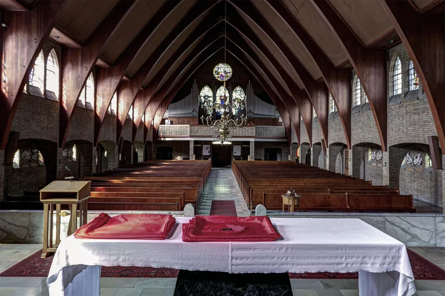 Altar table with two red books before the pews and organ gallery beneath timber roof beams.