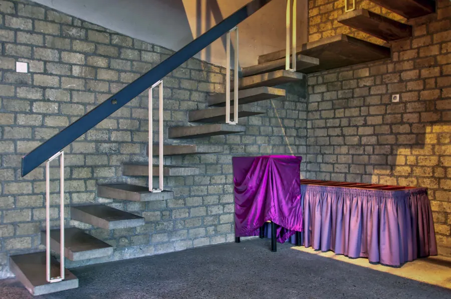 Open concrete staircase along a brick wall above purple-covered furnishings.
