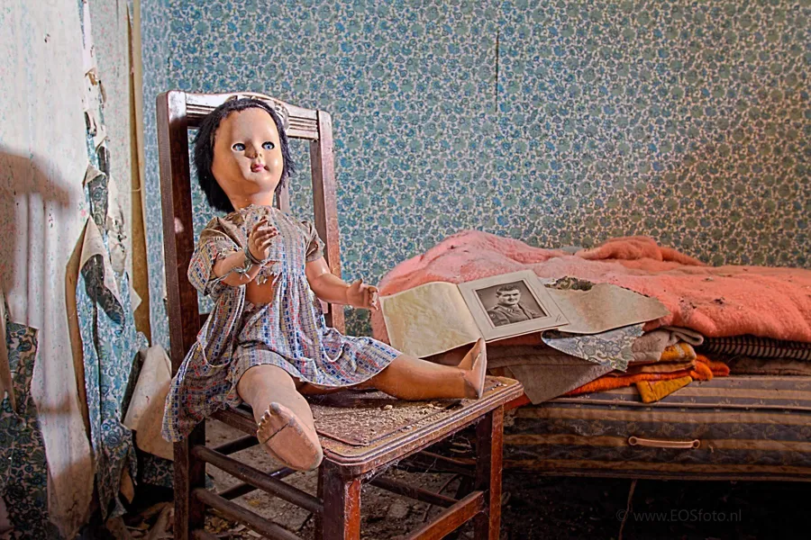 Doll on a wooden chair beside a bed with blankets and loose papers