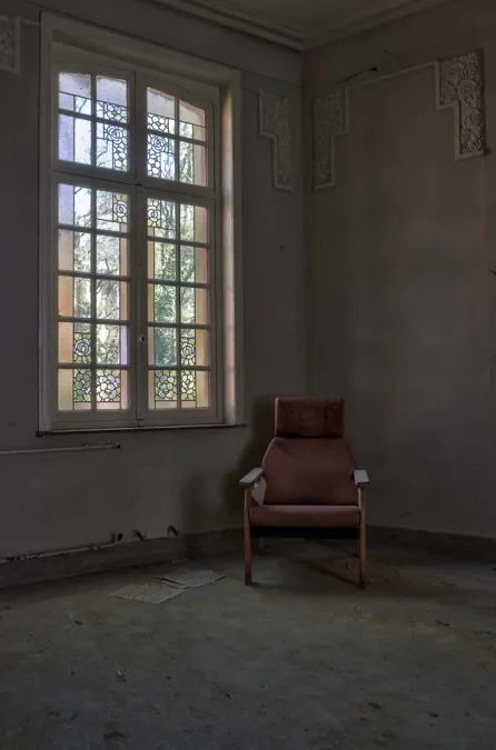 Chaise isolée près d’une haute fenêtre dans une pièce vide.