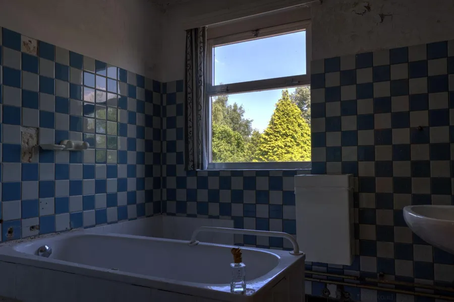 Badewanne unter einem Fenster zwischen blauen und weißen Fliesen.