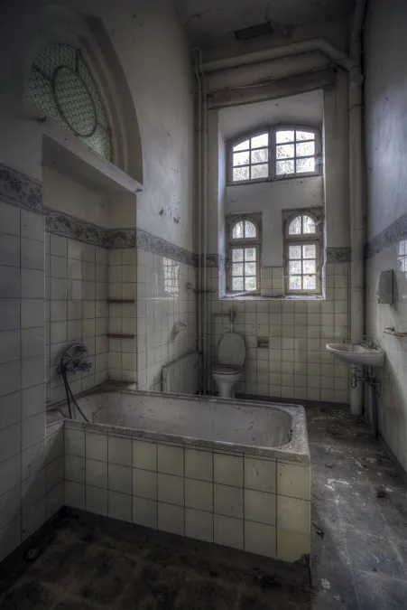 Bañera blanca en baño pequeño bajo una ventana alta.