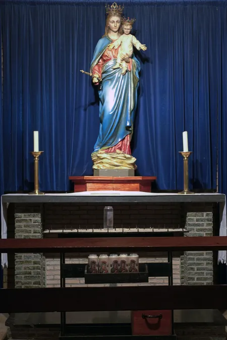 Statue of Mary with the Child on an altar before a blue curtain, flanked by candles.
