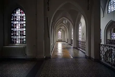Long gallery with pointed arches, coloured window left and metal balustrade right.