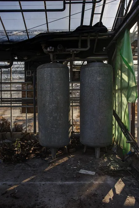 Twee hoge grijze tanks tussen leidingen in de kas.