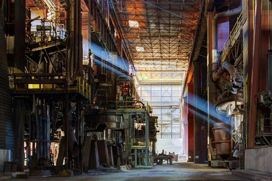 Blue shaft of light through a tall hall filled with pipes and machinery.