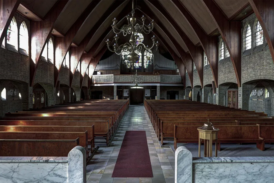 Symmetrical view from the altar along wooden pews towards the rear gallery, with chandeliers overhead.