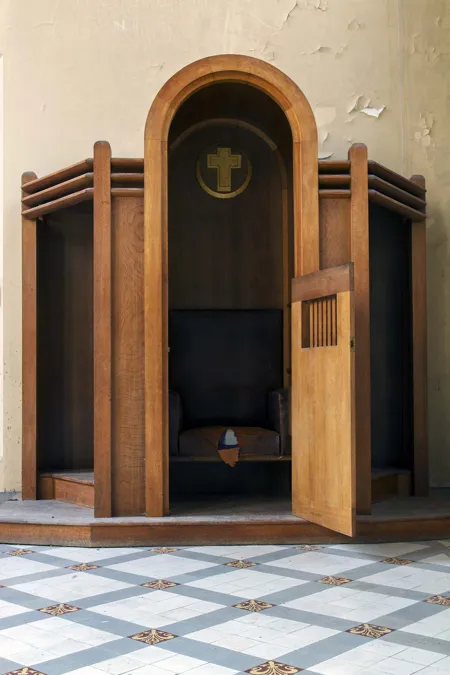 Confessionnal en bois à porte ouverte, avec croix au-dessus du siège.