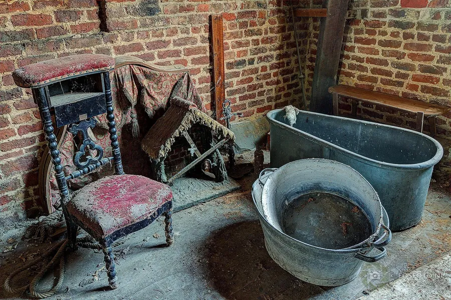 Versleten stoel en metalen waskuipen bij een bakstenen muur