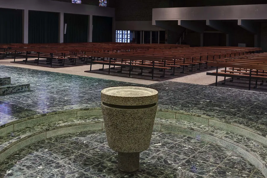 Round granite baptismal font in a lowered circular area before the pews.