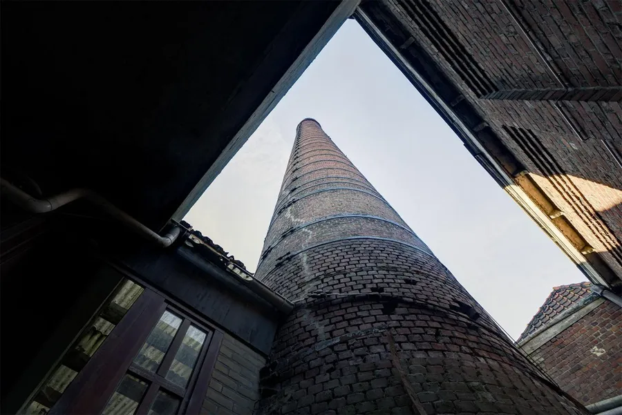 Chimenea alta redonda de ladrillo vista desde abajo entre edificios.