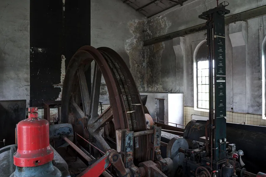 Große Seiltrommel neben hoher Messskala und rotem Maschinenbauteil.