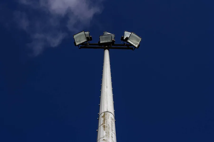 Vista hacia una torre blanca alta con cuatro focos contra cielo azul intenso.