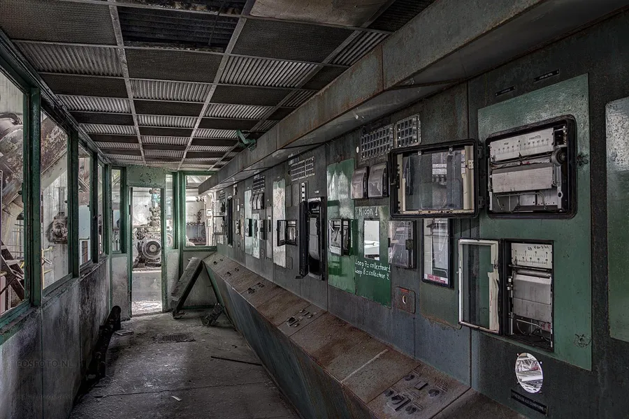 Long row of green control panels with gauges along a window wall.
