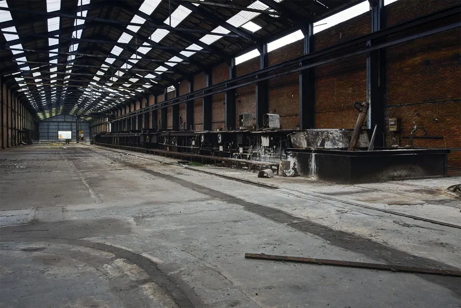 Lange bijna lege fabriekshal met daklichten.