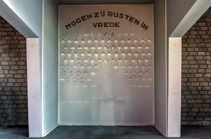 Memorial wall with small crosses beneath Dutch words wishing the departed peace.