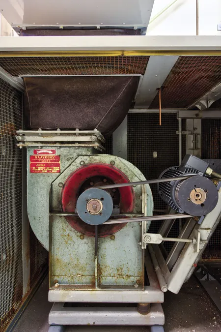 Oude ventilator met rode riemschijf en aandrijfriemen in een houten omkasting.
