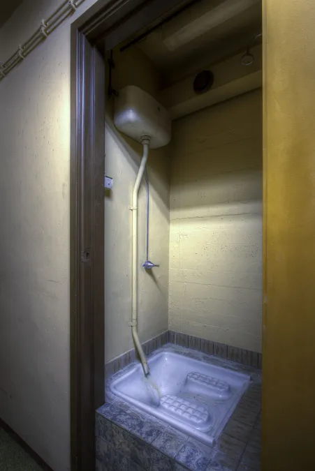 Smalle douchecabine met witte douchebak en een douchekop hoog aan de wand.