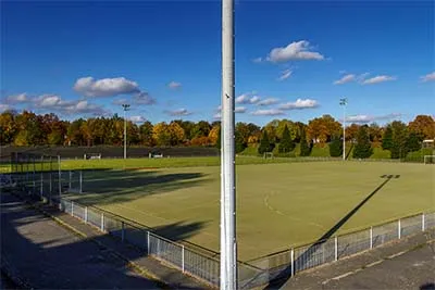 View from the stand over an empty field, with a lighting mast in front and long shadows.