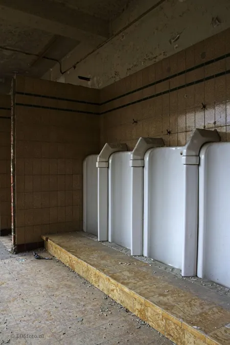 Reihe weißer Urinale vor beschädigten gefliesten Wänden.