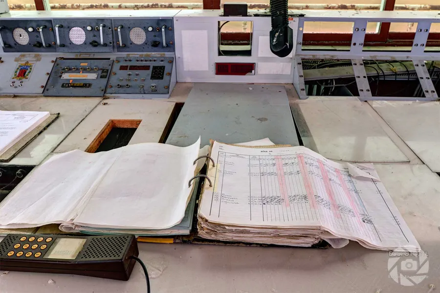 Open logbooks and papers before an old control panel with round gauges.
