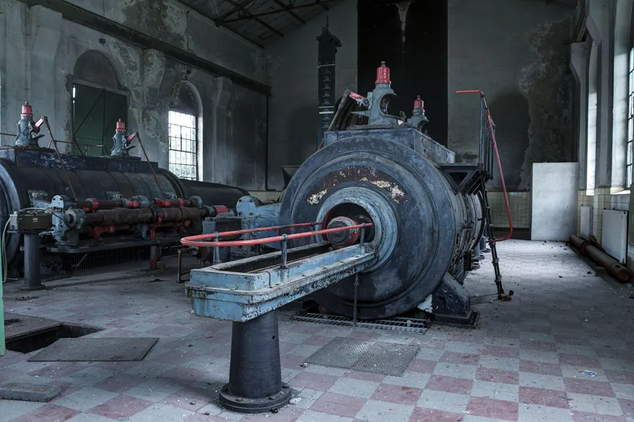 Große Fördermaschine mit rundem Zylinder und roter Bedienung auf kariertem Boden.