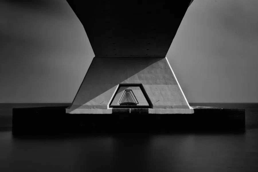 Vue en noir et blanc sous le pont de Zélande, avec une large pile en béton et les suivantes fuyant au centre.