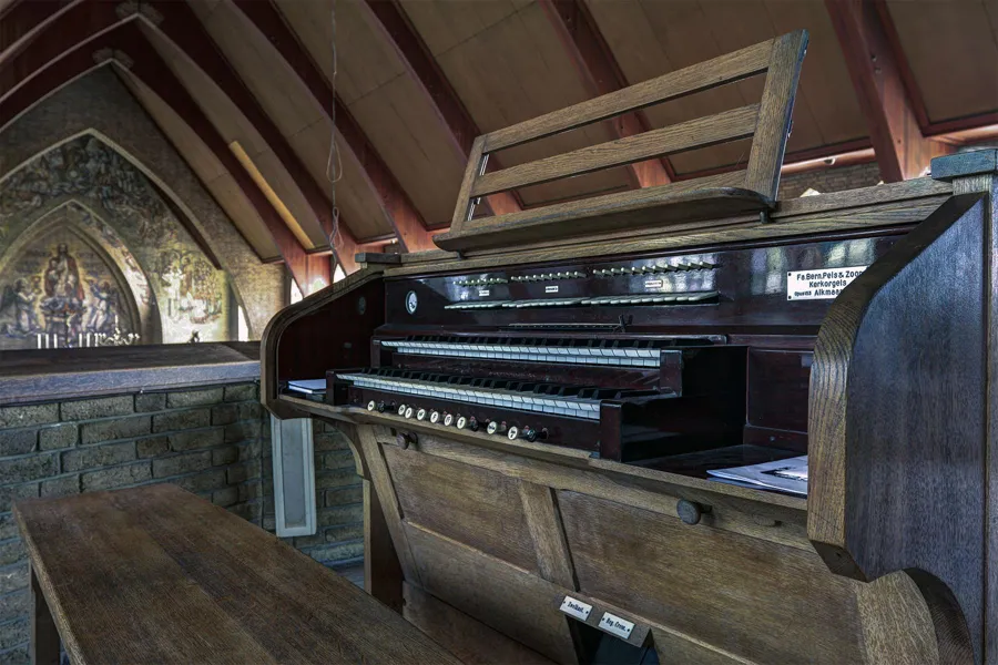 Wooden organ console with two keyboards and an empty music stand beneath sloping roof beams.
