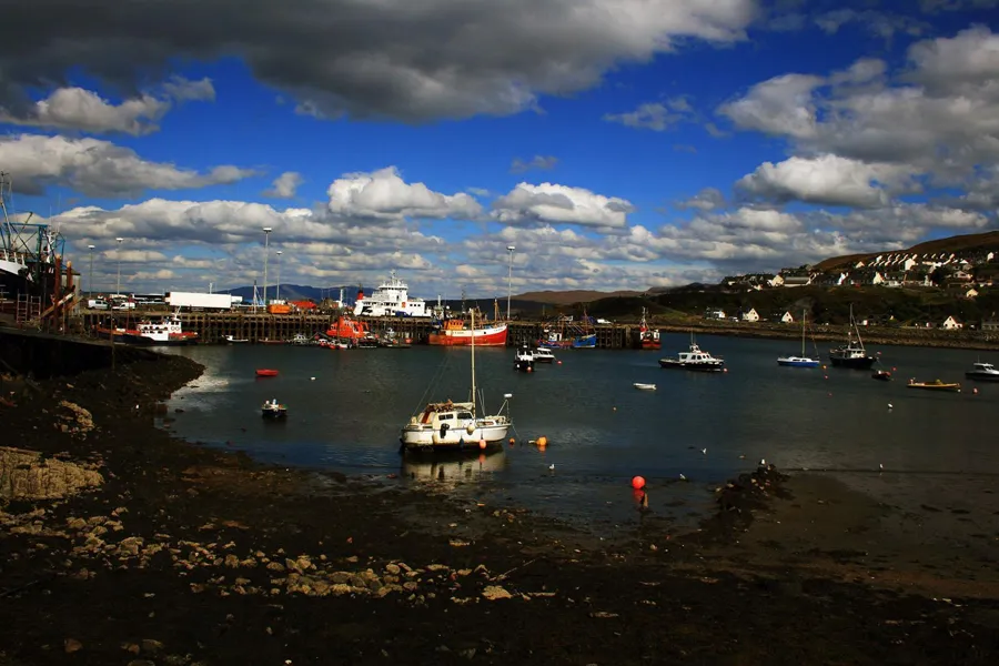 Hafen von Mallaig mit Booten, großer Fähre am Kai und Gebäuden am Hang.