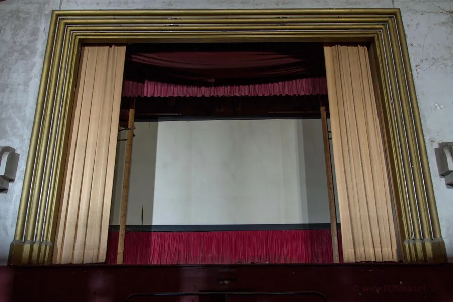White projection screen between beige curtains with a red lower border.