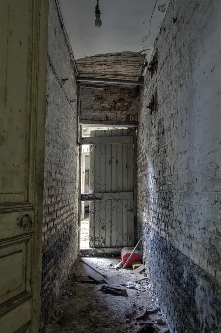 Narrow decaying passage leading to a wooden door.