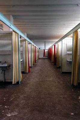 Long corridor between small partitioned spaces with coloured curtains.