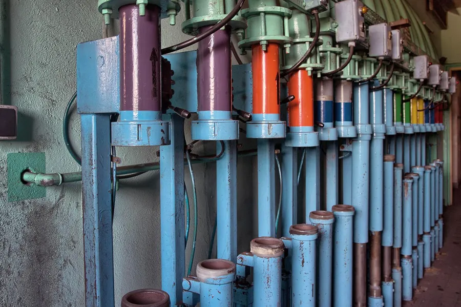 Rij gekleurde cilinders in blauwe houders aan de wand.