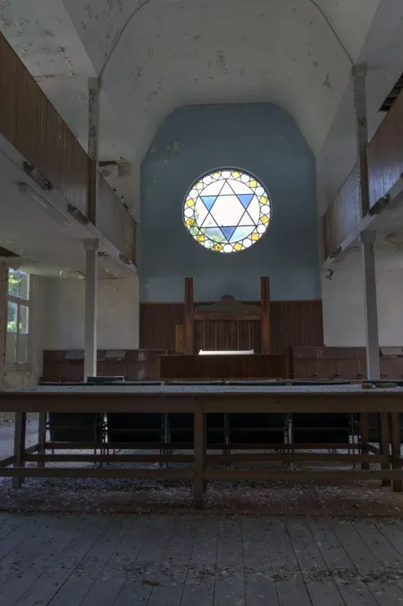 Tall synagogue interior with wooden benches and a Star of David in a round window.