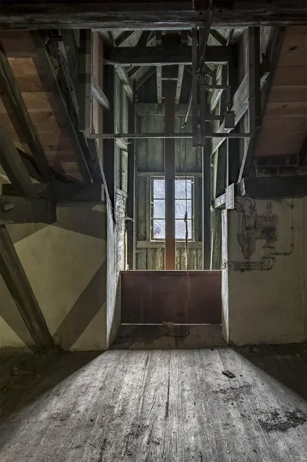 Hölzerner Dachboden entlang einer hohen Maschinenkonstruktion mit kleinem Fenster am Ende.
