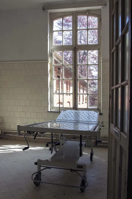 Table d’examen à roulettes dans une pièce carrelée à haute fenêtre.