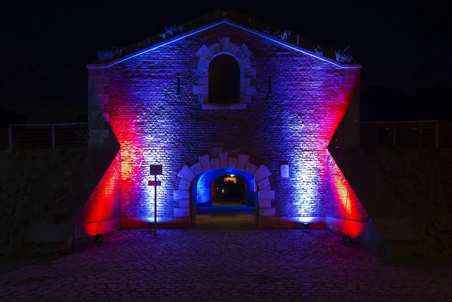 Symmetrisch gebouwtje met centrale boogpoort in rood en blauw licht.