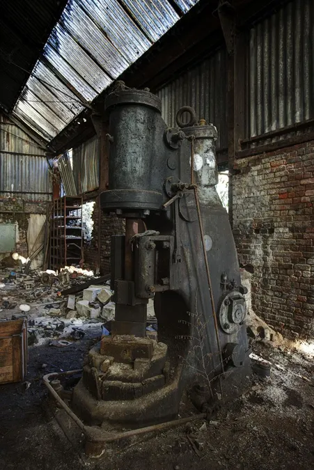 Machine lourde rouillée à cylindre vertical près d’un mur en briques.