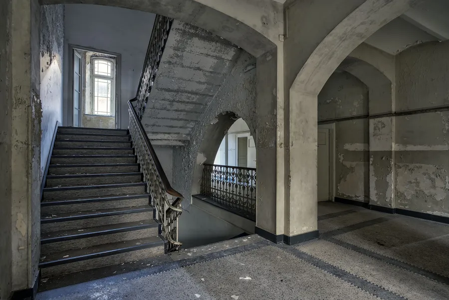 Escalera ancha de hormigón bajo arcos con barandilla metálica decorada.