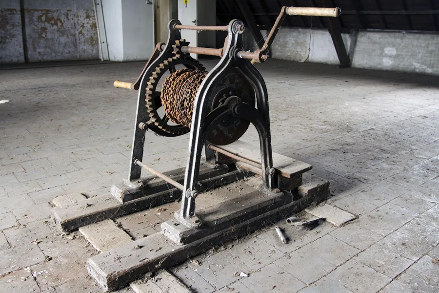 Oud metalen windwerk met slingers en tandwielen op een houten vloer.