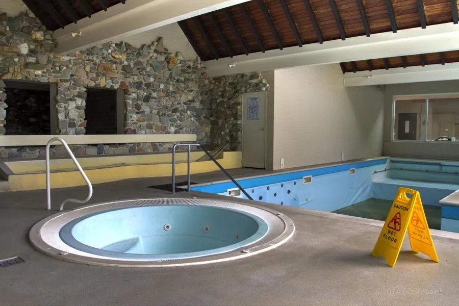 Jacuzzi redondo vacío junto a la piscina y un cartel amarillo.