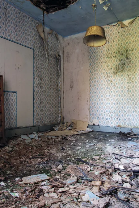 Decaying room with a small yellow pendant light and rubble on the floor.