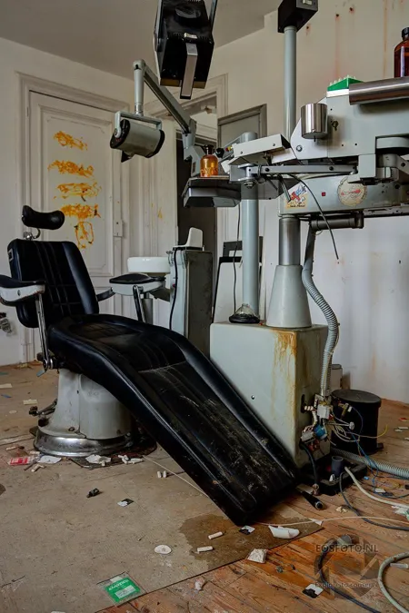 Black reclining dentist’s chair among abandoned equipment.