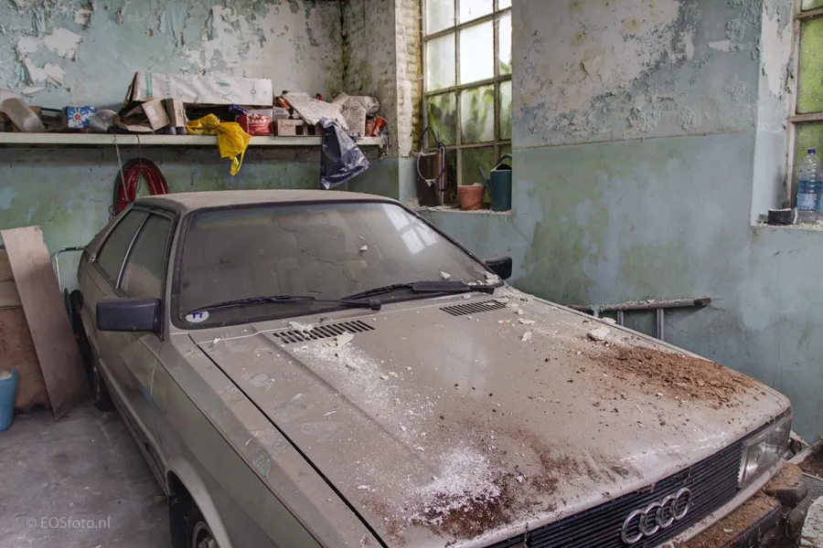 Coche polvoriento en un garaje con paredes desconchadas