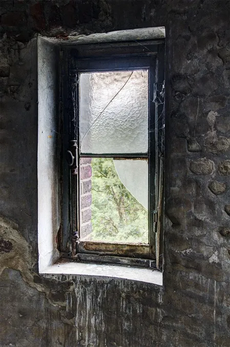 Ventana pequeña desgastada en muro oscuro de piedra del desván.