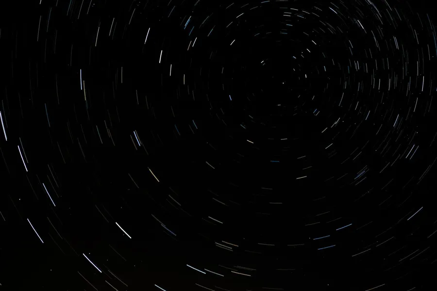 Weiße und hellblaue Sternspuren bilden konzentrische Bögen am dunklen Himmel.