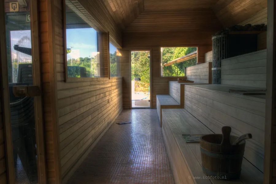 Lange Holzsauna mit Bänken rechts und Eimer mit Kelle vorne.