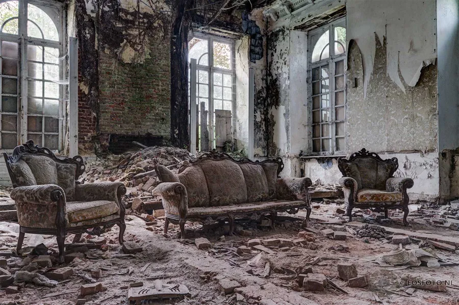 Upholstered seating among rubble beside tall arched windows